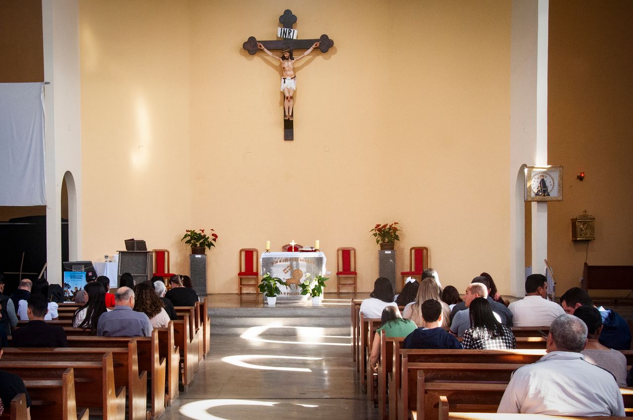 An interior view of a church with a congregation attending a religious service with a prominent crucifix.