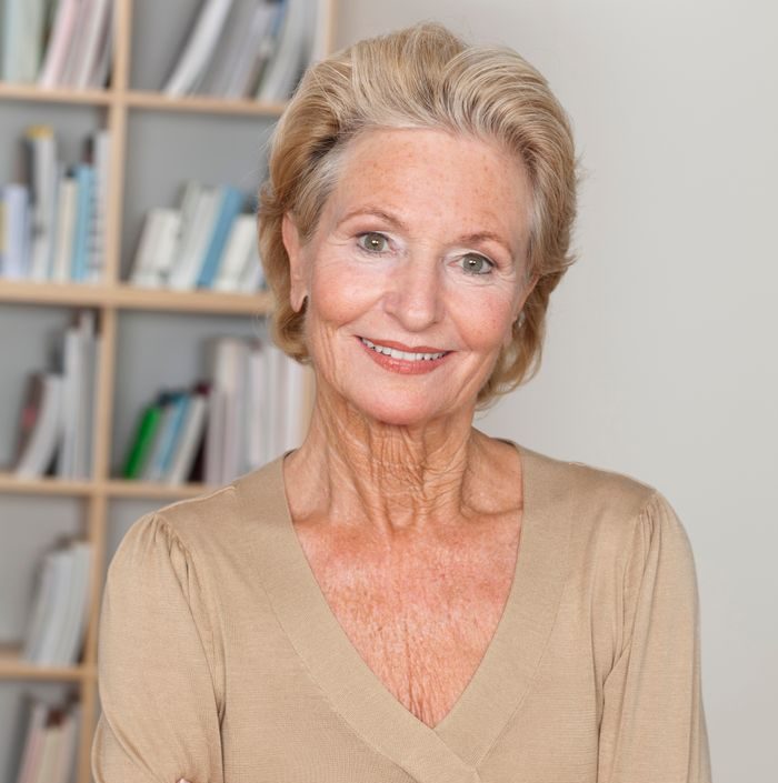 Confident senior woman indoors with crossed arms and a warm smile.