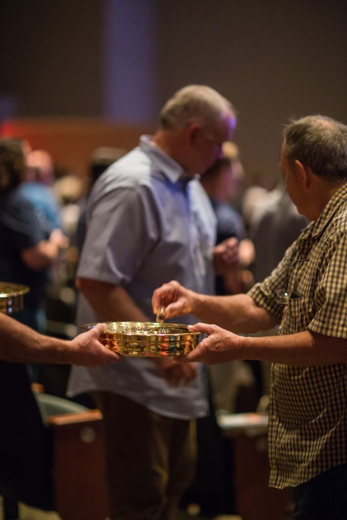 Worship Services Men exchanging collection plates during a church service indoors.